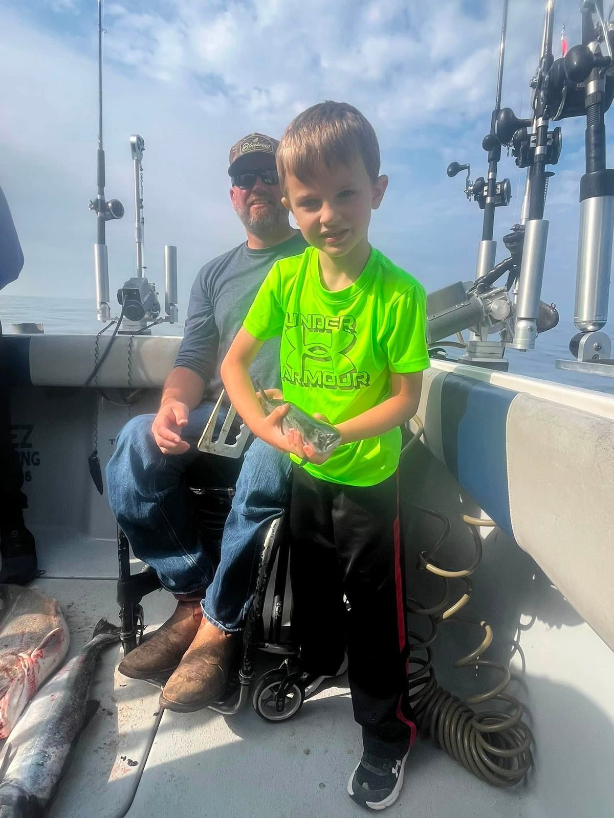 A young child in a bright green shirt on the deck of the charter boat, supervised by an adult, with rods and equipment visible