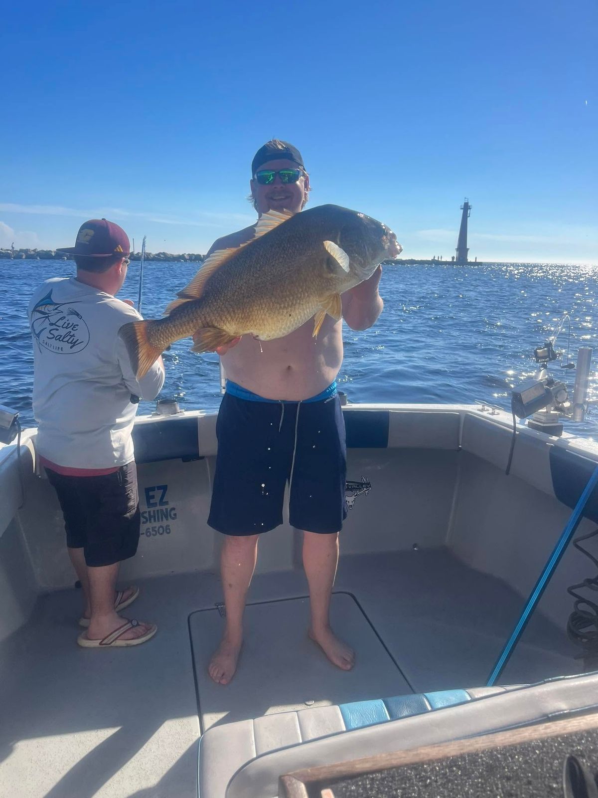 An angler displays a large fish with the Muskegon lighthouse visible behind the boat