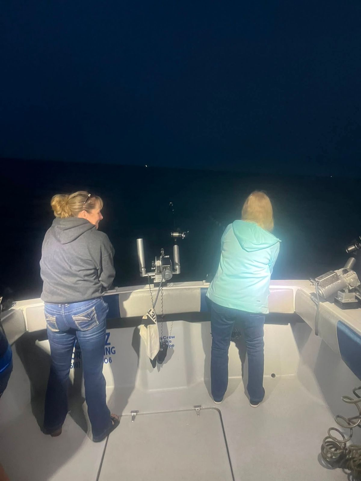 Two anglers fish at night from the stern of the Too Ez charter boat