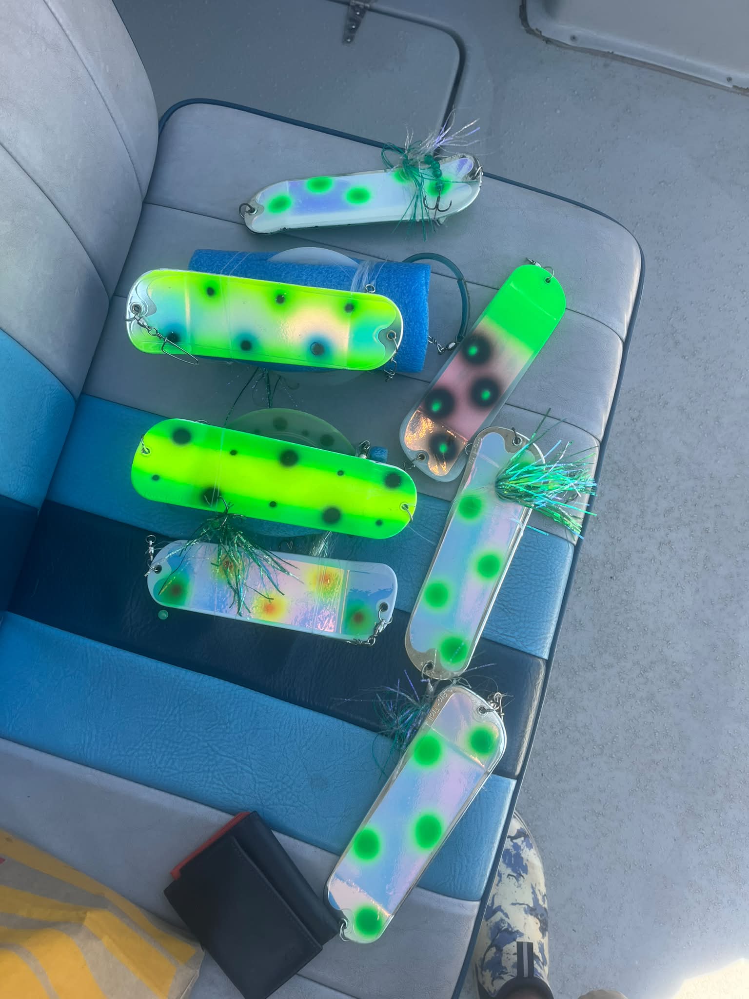 A collection of colorful fishing lures with bright green and fluorescent patterns, displayed on a boat seat.