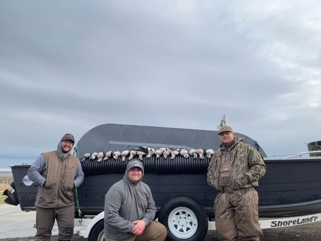 Three fishermen pose with a large catch of white fish displayed on a black boat trailer.