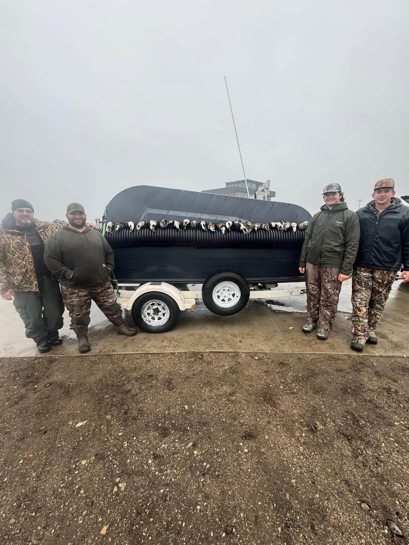 Five anglers pose proudly with a large catch of white fish displayed on the side of a black fishing vessel or transport trailer.