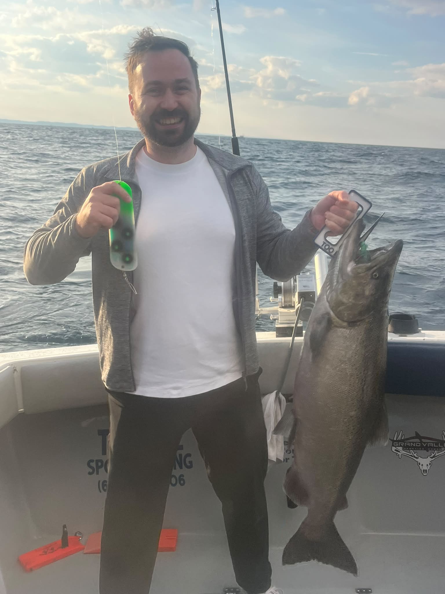 A satisfied customer holds a large lake trout catch aboard a Too Ez Sportfishing charter boat on open water.